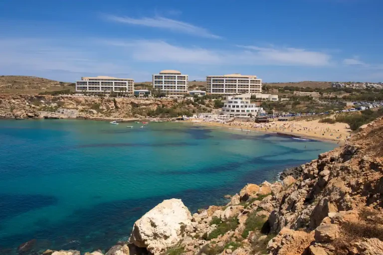 Playa de arena Golden Bay en Malta, con hoteles frente al mar y aguas turquesas.