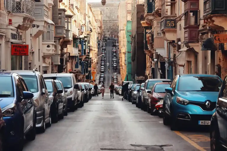 Calle estrecha con coches aparcados en La Valeta, Malta — ejemplo típico del tráfico y estacionamiento en la isla.