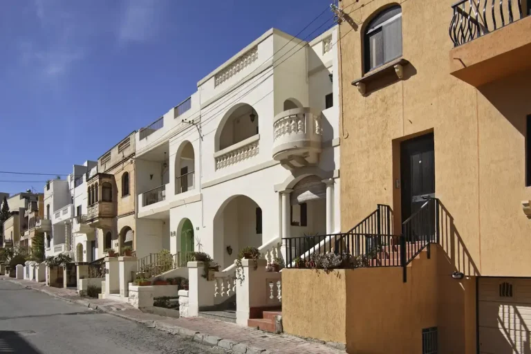 Fila de casas residenciales típicas de Malta con balcones y fachadas de piedra, representando el estilo de vivienda para alquiler de larga duración.