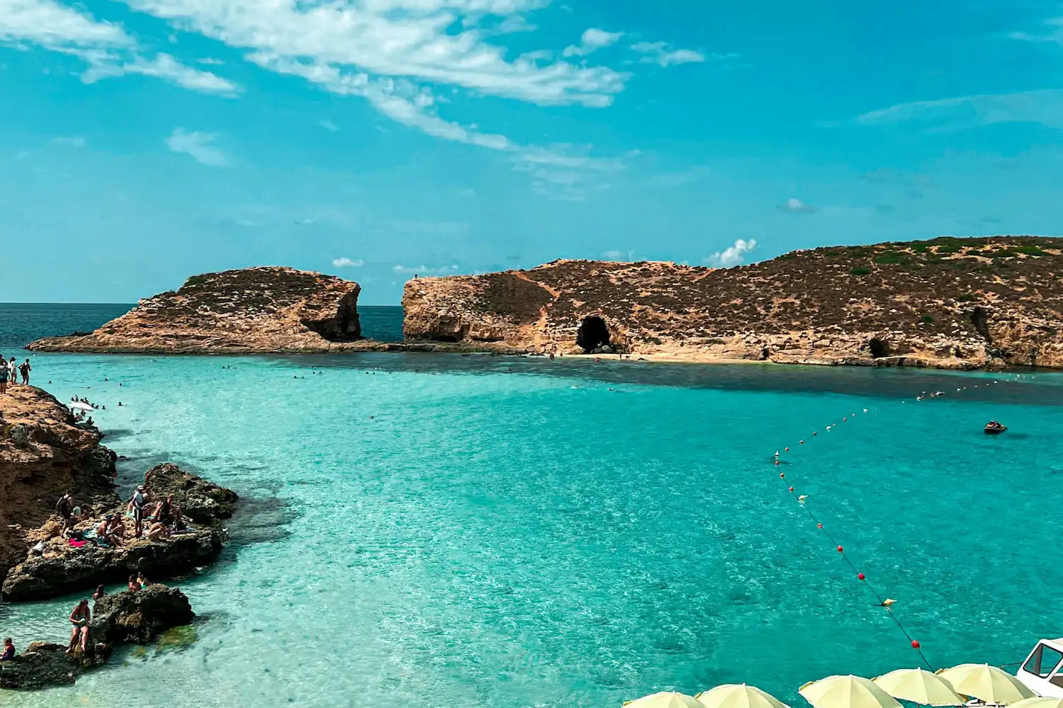 Blue Lagoon en la isla de Comino con agua turquesa, costa rocosa y visitantes bañándose durante la temporada de verano