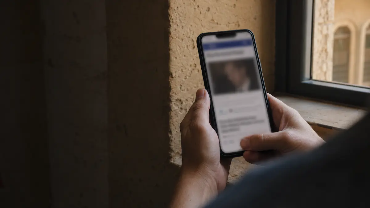 Una persona consulta en su teléfono móvil un artículo de noticias desenfocado con la fotografía de alguien no identificado.
